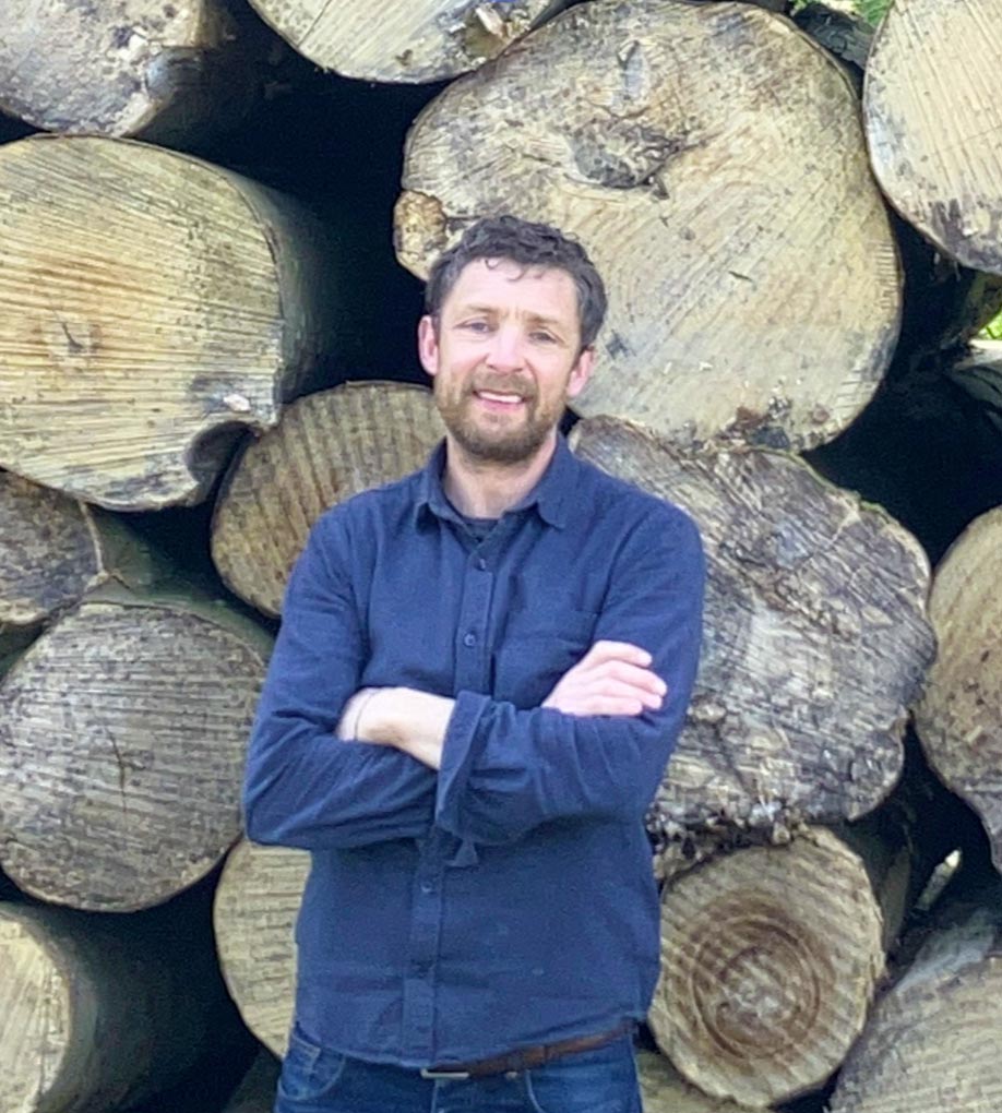 Portrait of Will Salvetti, founder of LBS, standing in front of a stack of timber.